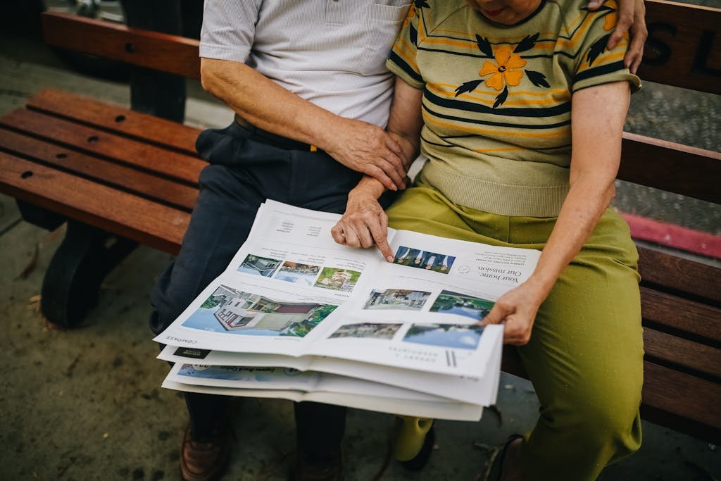 Elderly couple sitting outdoors, reading and embracing on a park bench.